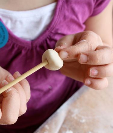 overhead photo of girl's hands poking hole in salt dough bead