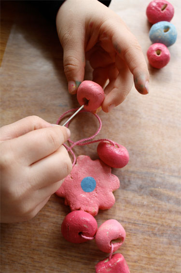 girl's hands threading salt dough beads with needle 
