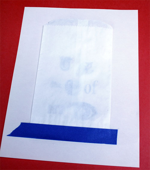 securing white sandwich bag onto printable paper with blue tape