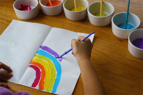 child painting a rainbow onto paper 