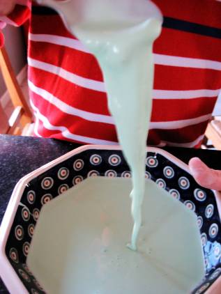 green oobleck in a bowl and pouring off of a spoon into the bowl