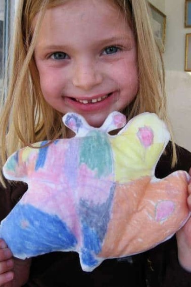 child holding fabric stuffed butterfly made with their drawing