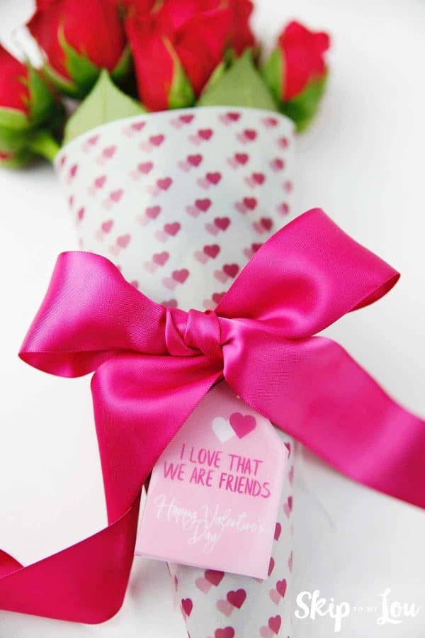 free printable flower wrap with paired hearts printed on it, wrapped around long seemed red roses, with a fuchsia pink bow wrapped around it and a Happy Valentine's tag attached