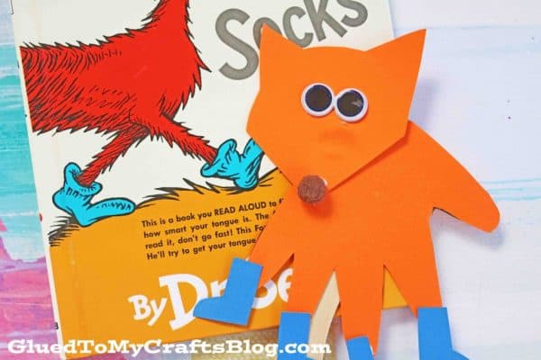 orange fox with blue socks puppet with the book fox in the socks book behind it to celebrate dr Suess