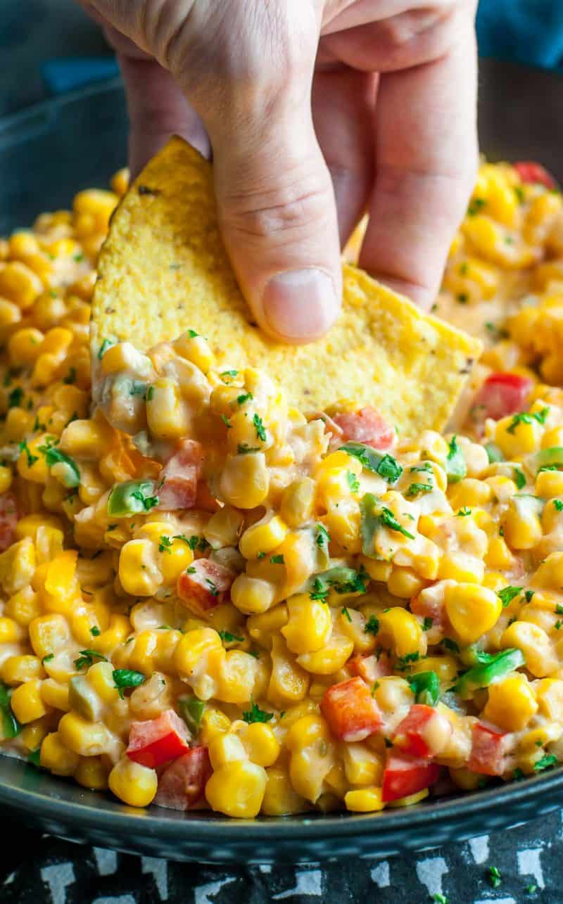 hand scooping up corn dip on a tortilla chip