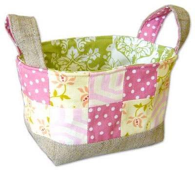 Pretty fabric basket that has pink and white polka dot, yellow floral, yellow with pink lines fabric squares sewn together, with a green and white fabric lining the inside of the basket with a canvas bottom and canvas and pink polka dot handles