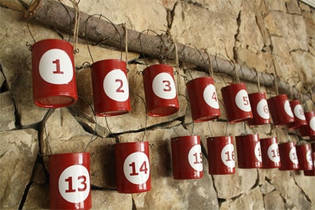 Recycled can painted red with white circle and red number in the center. they are hung with a wire loop tied with twine for second level attached to a branch