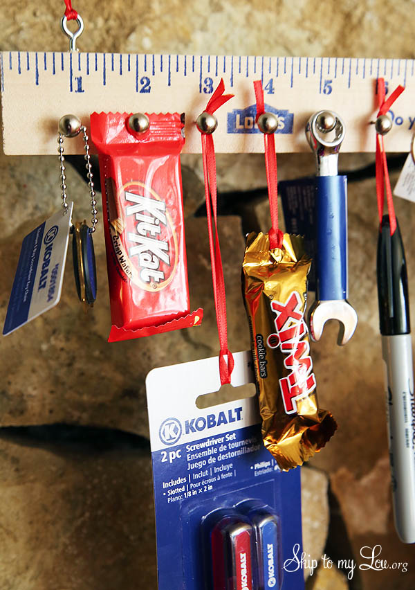 Wooden yardstick advent calendar for boys with tools, chocolates, and other things hanging from it.