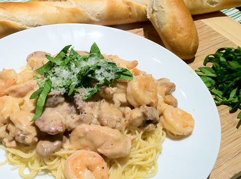 Fishbones-Cajun-Pasta-Recipe Cajun Pasta with sausage and shrimp and angel hair pasta served on a white plate with a baguette.