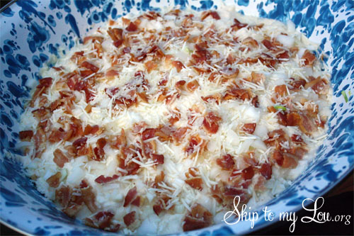 Bacon, onion and parmesan cheese topped cauliflower salad in a blue and white bowl ready to be served.