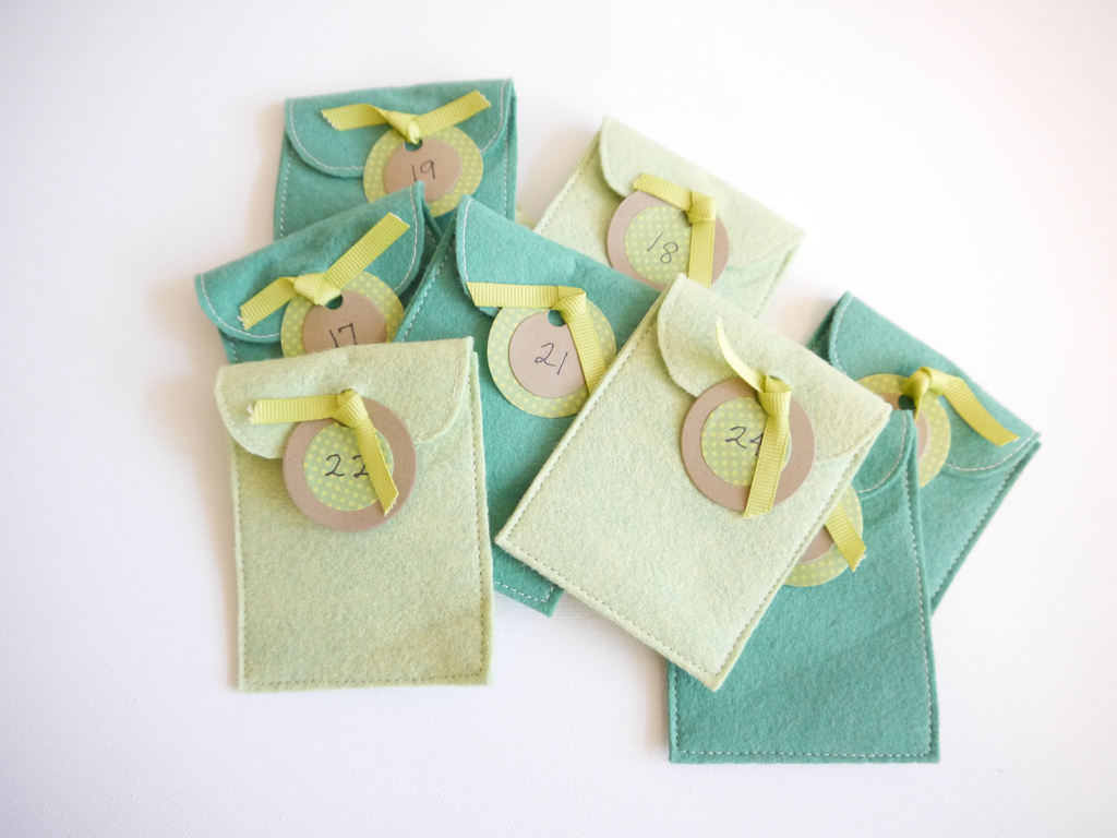Multiple pockets for the Felt Advent Calendar in pastel teals and light green with date tags tied on with yellow ribbons.  -Skip To My Lou