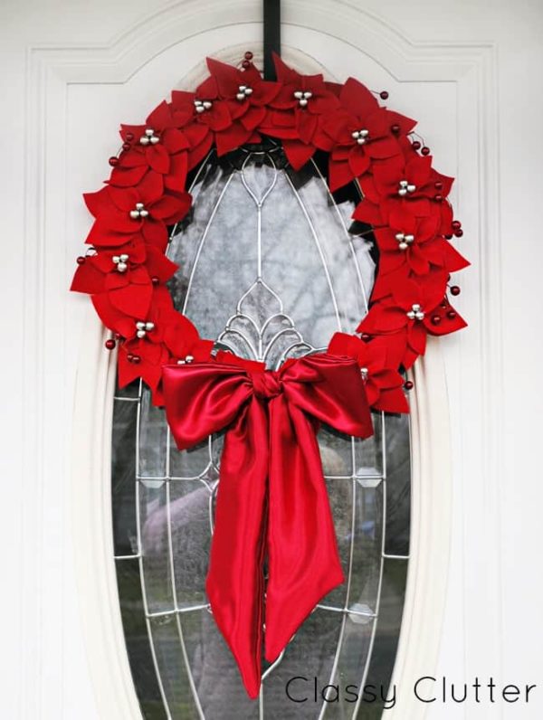 Image shows a felt Poinsettia Wreath hanging from a white door. - Classy Cutter