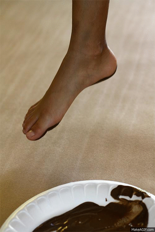 A child's foot being placed in brown paint that is on a disposable plate; once dipped the foot is placed on the contractor paper creating the head of the reindeer