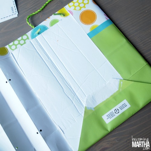 The gift bag is opened up showing holes punched in the folded spine portion. A yarn handle is attached through punched hole.
