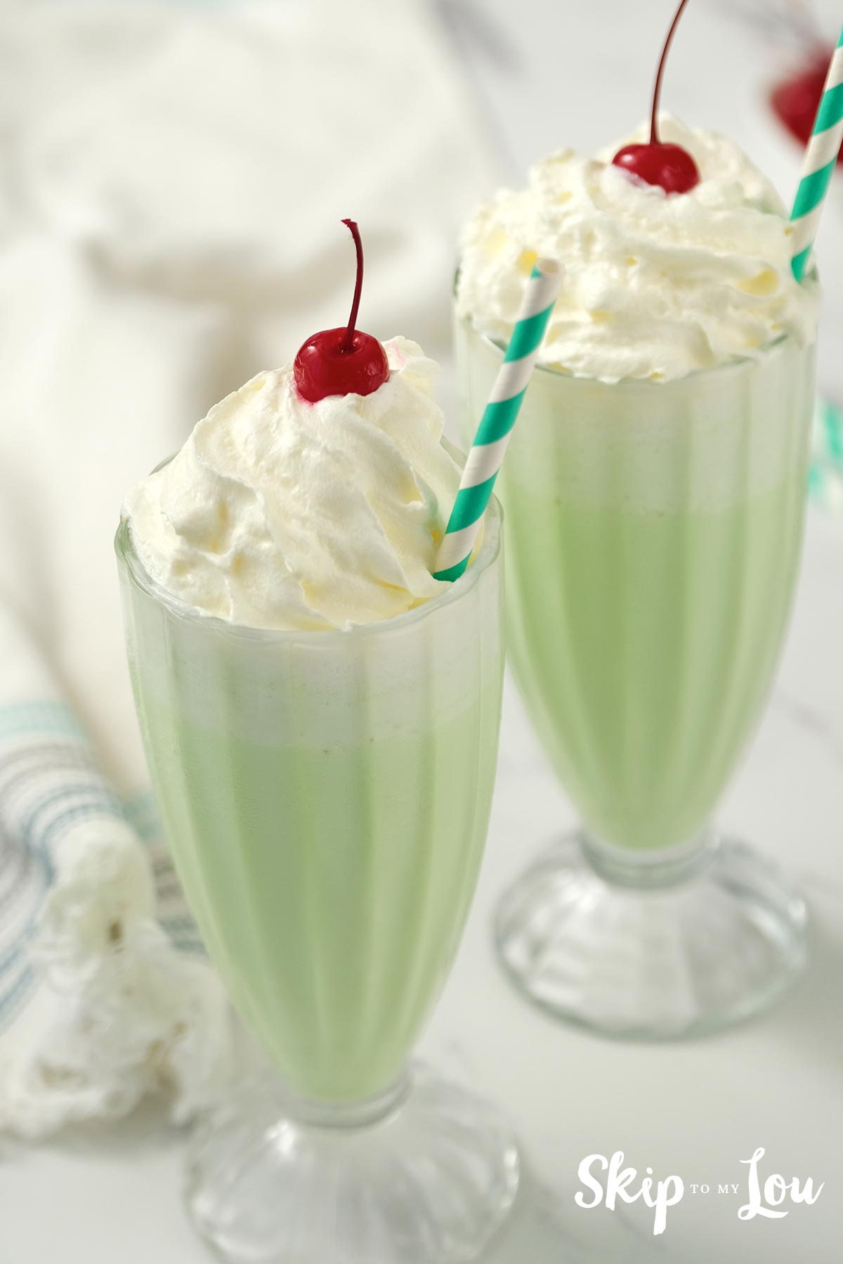 shamrock shake in tall sundae glass with green and white straw and whipped cream and a cherry