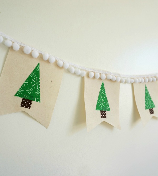 Canvas Christmas tree banner handing on wall. Banner has white pom poms on top.