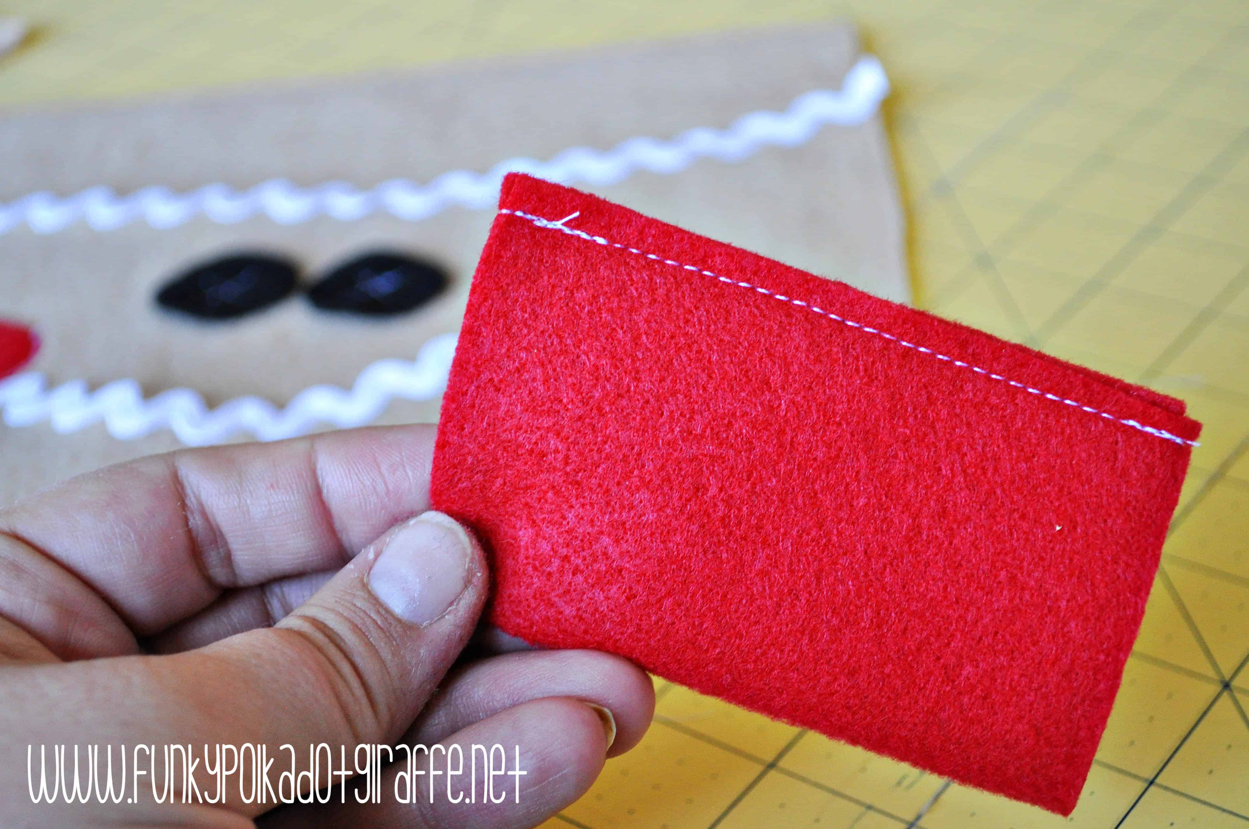 WWW.FUNKYPOLKADOTGIRAFFE.NET A scrap of red felt being held to show how to start making a bow for the gingerbread purse. -Skip To My Lou