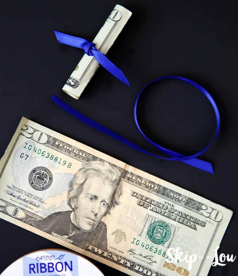 diy money diploma - a twenty dollar bill with blue ribbon beside it and another twenty dollar bill with blue ribbon wrapped around it making the diploma