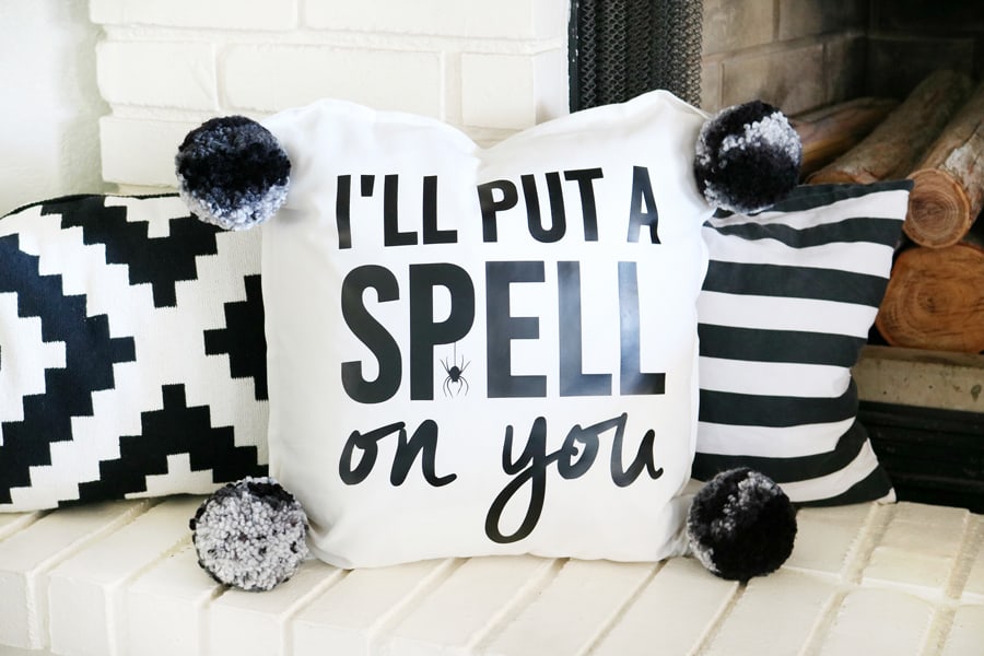 I'll put a spell on you pillow; the pillow is white with black letters and is decorating a white bench with tow other black and white decorative pillows