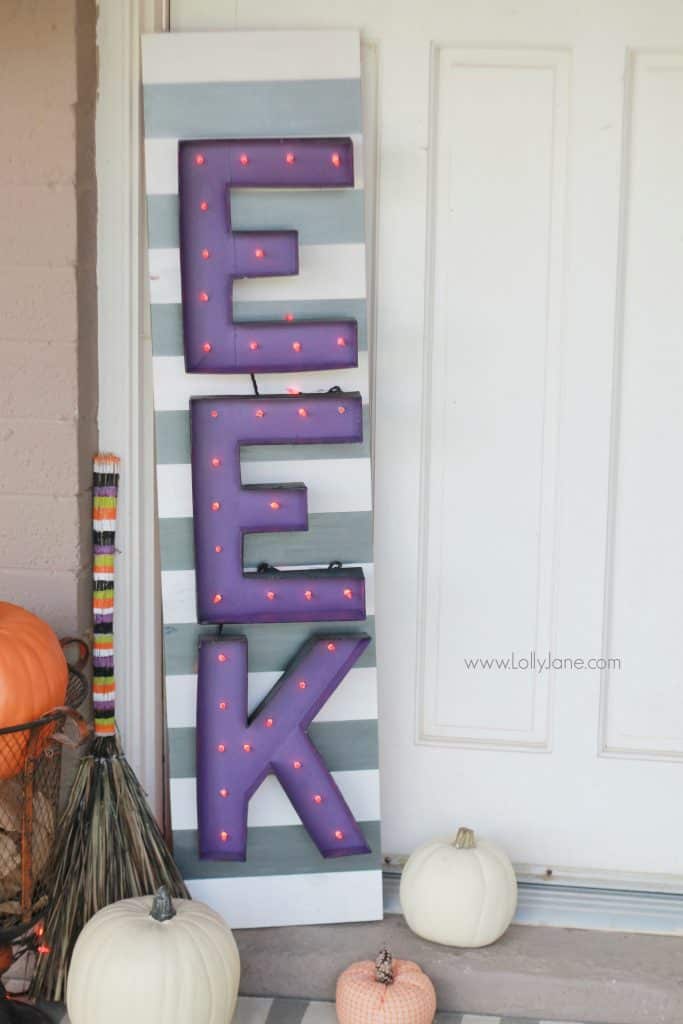 EEK Porch Halloween sign with the letters painted with purple and orange paint on a gray and white striped backing