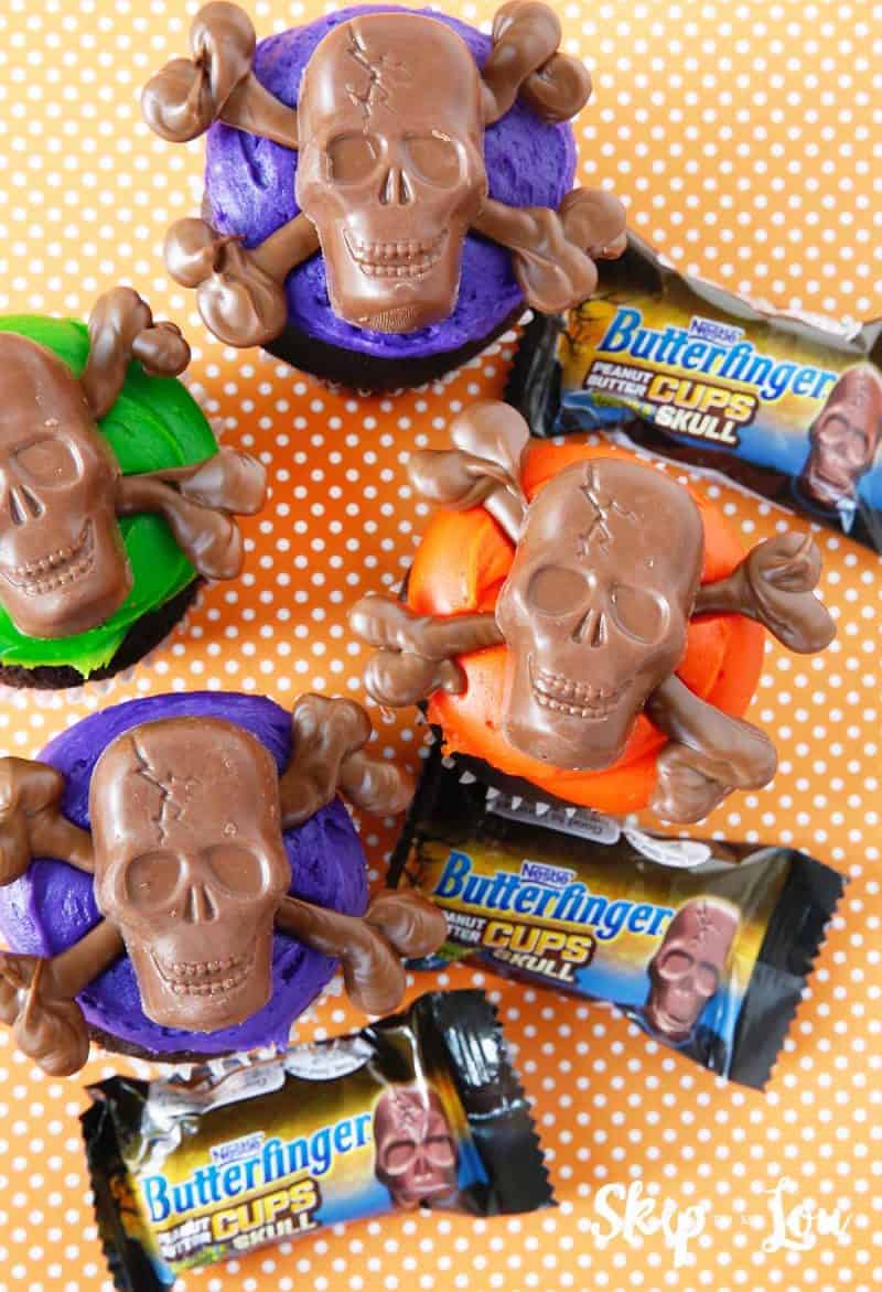 skull and crossbones cupcakes with butterfinger bite size candies on an orange with white polka dot background