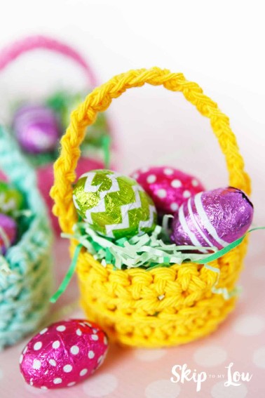 yellow crochet basket filled with fake green grass and three foiled wrapped mini chocolate eggs