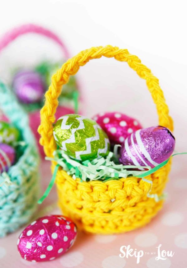 yellow crochet basket filled with fake green grass and three foiled wrapped mini chocolate eggs
