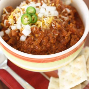chili recipe in bowl with onions jalpenos crackers on the side