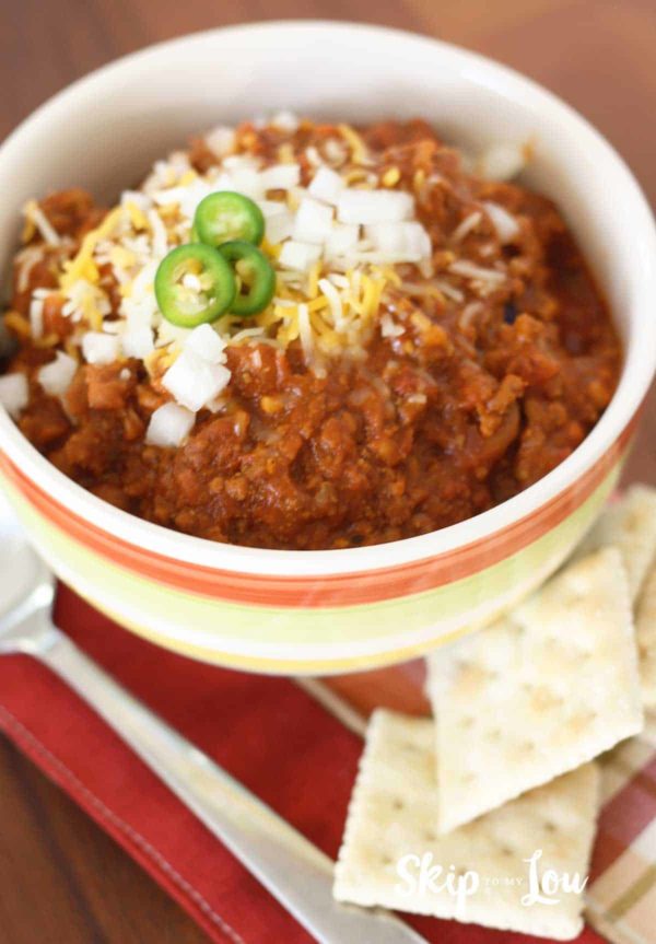 chili recipe in bowl with onions jalpenos crackers on the side