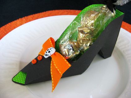 black with green interior witch shoe treat container; there are orange buttons and a orange ribbon with a skull decorating  the top of the shoe