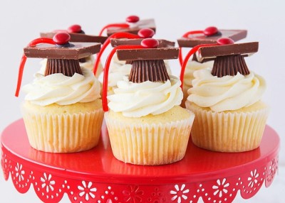 white cupcakes with white frosting and candy grad hat with red tassel on red cake stand