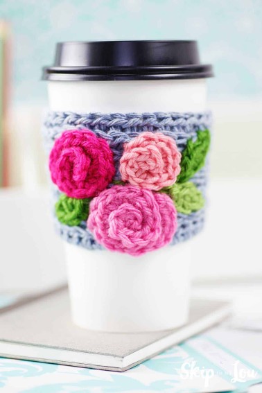 crochet coffee sleeve with roses on white take out cup sitting on desk