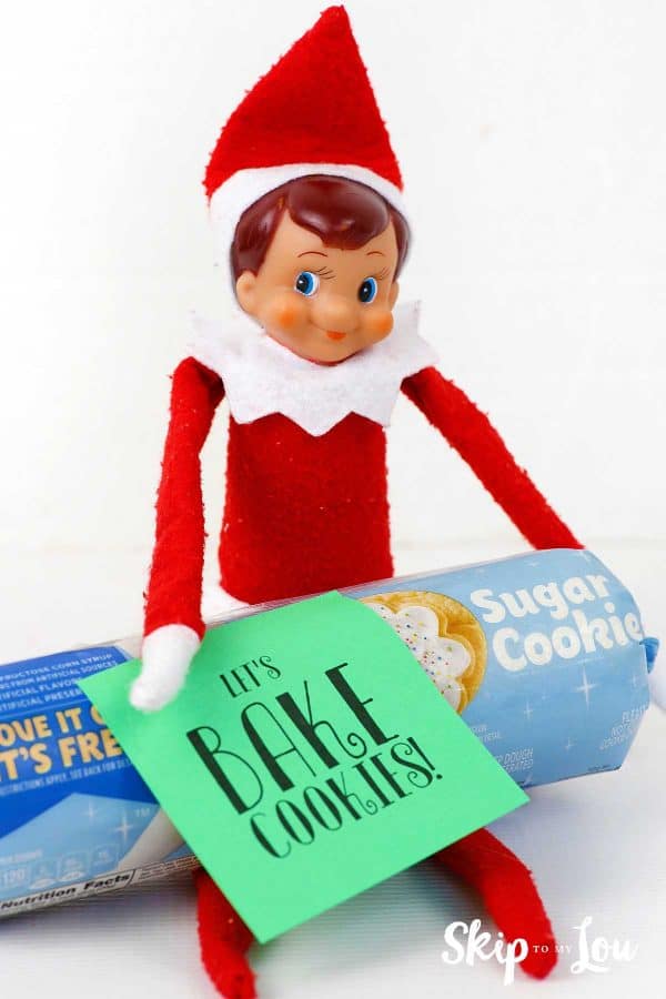 Elf on the shelf holding a tube of sugar cookie dough with a green post it note, "Let's bake cookies!" -Skip To My Lou