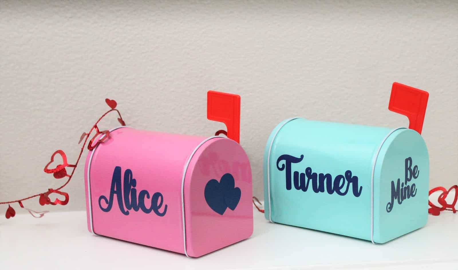 pink metal mail box with red flag that has the name Alice and hearts on it, and a light blue mail box with red flag with the name Turner on it and the words be mine