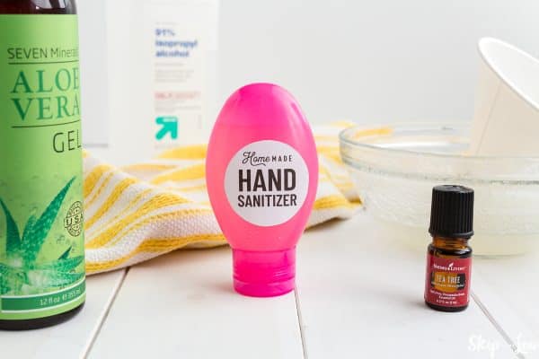 hand sanitizer in pink bottle with white circle label  yellow towel aloe vera essential oils mixing bowl in background