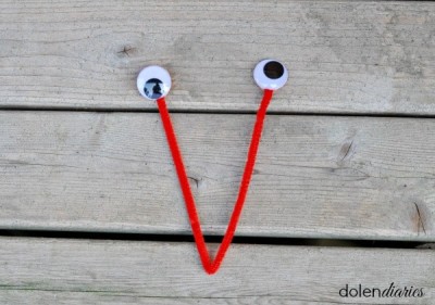 Red pipe cleaner folded into a V with wiggly eyes attached to the two ends