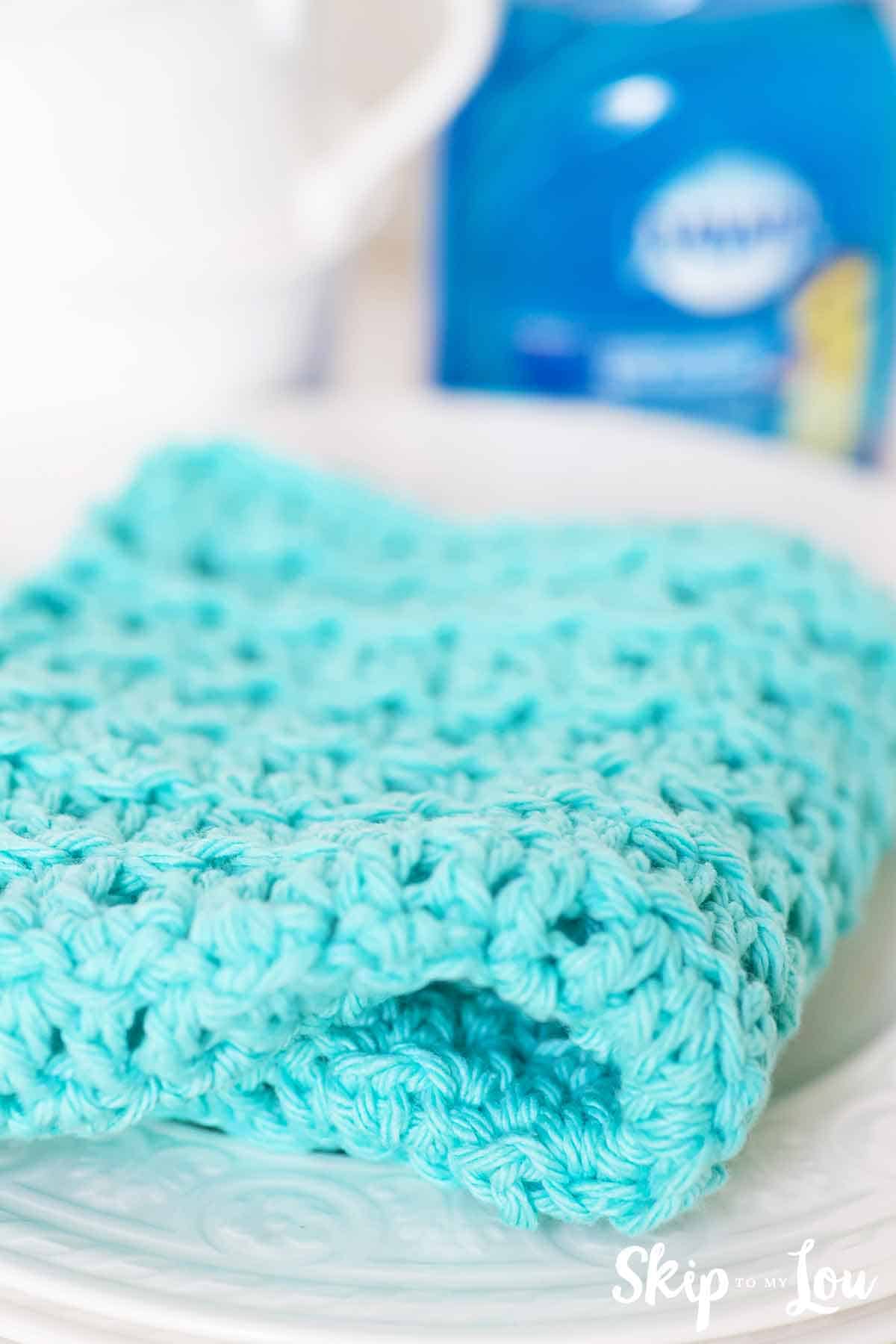 floret crochet dishcloth on stack of white plates and dish soap in background