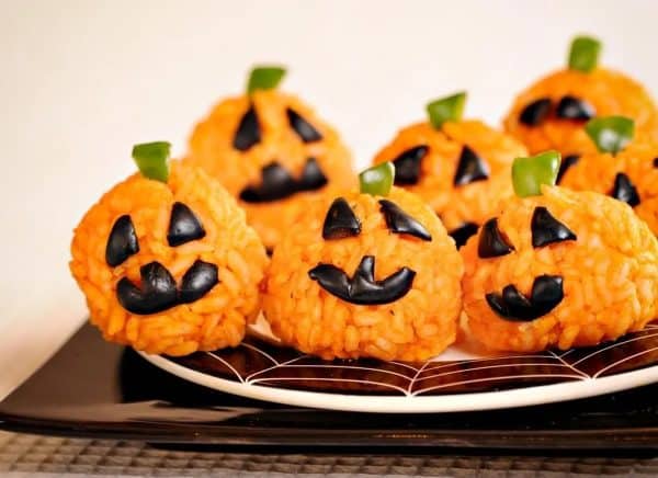 Image shows 6 carrot rice jack-o-lantern on a plate for a Halloween dish.