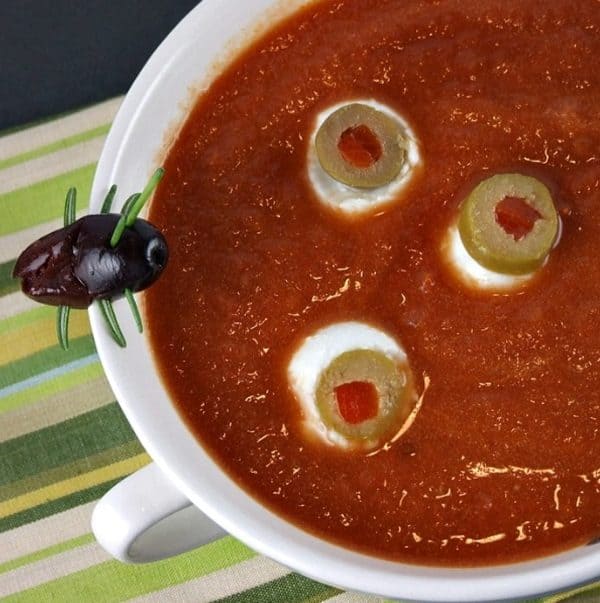 Image shows a soup decorated with olives to look like eyeballs and a bug decoration next to it.