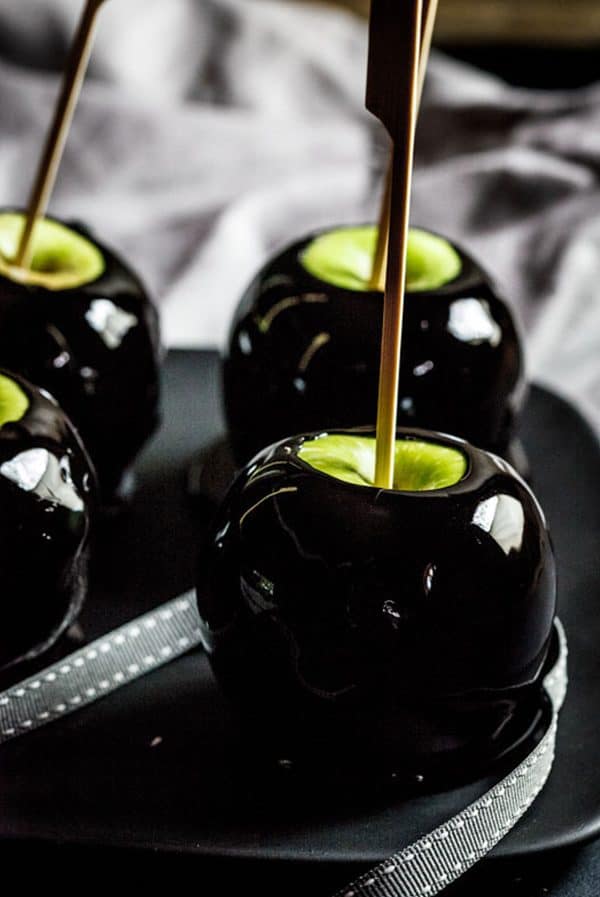 Image shows four apples covered in black candy for Halloween.