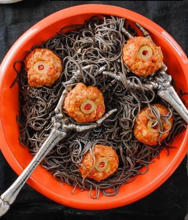 Image shows a black bean and meatball pasta with skeleton spoons.
