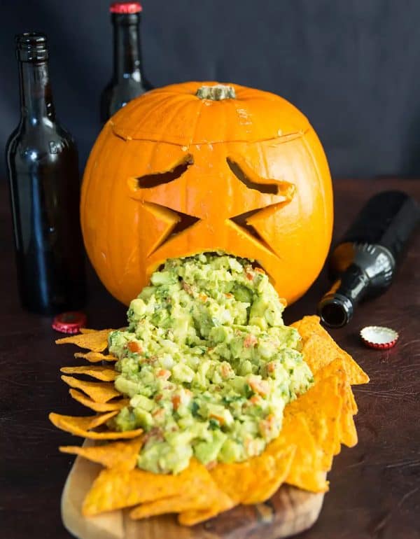 Image shows a puking pumpkin with guacamole and chips over a black background.