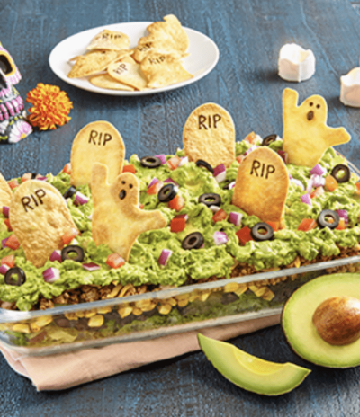 Image shows a Halloween guacamole that looks like a graveyad with chips shaped like graves and ghosts, next to avocado.