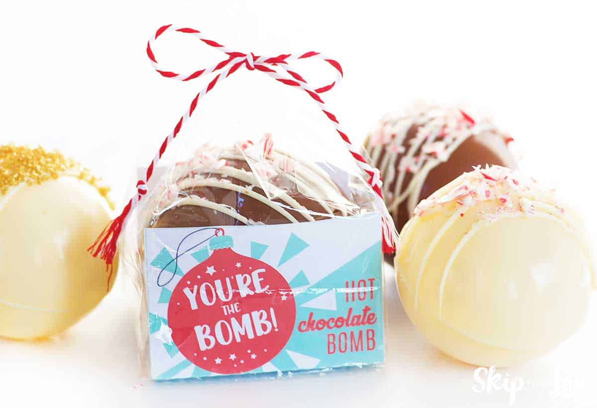 packaged cocoa bomb with white chocolate cocoa bomb topped with peppermint pieces sitting beside
