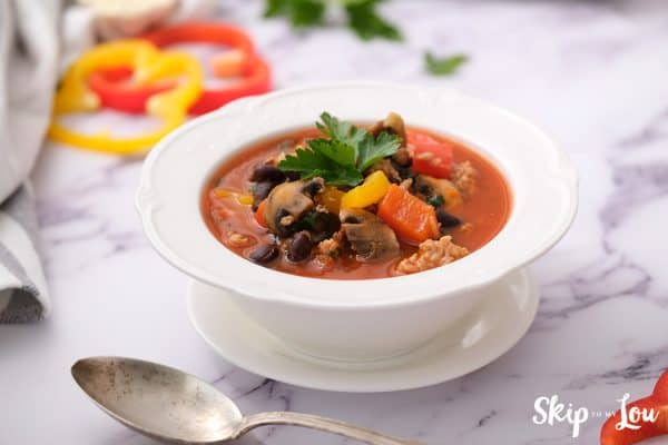 a white soup bowl full of weight loss soup garnished with cilantro in the middle sitting on a whte saucer with a soup spoon beside it