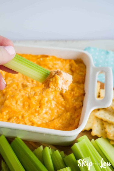 baked buffalo chicken dip in a white casserole dish and celery being dipped