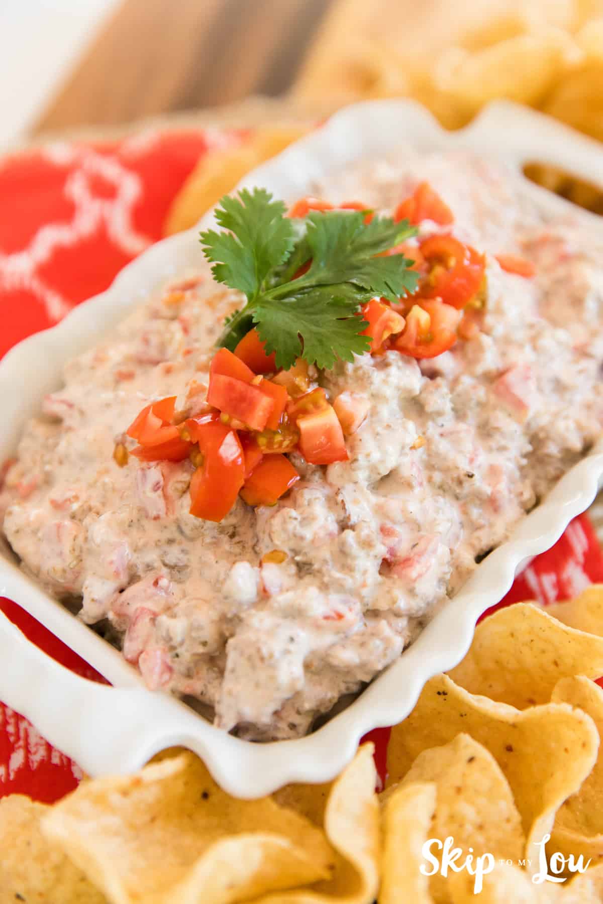 Rotel Sausage dip in white dish on red towel with tortilla chips around