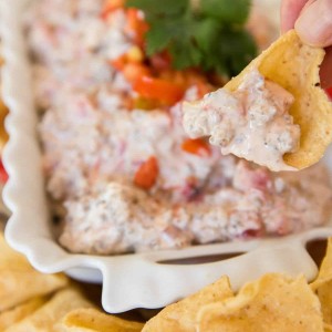 sausage rotel dip in white rectangle ceramic dish with hand holding chip scooping it up