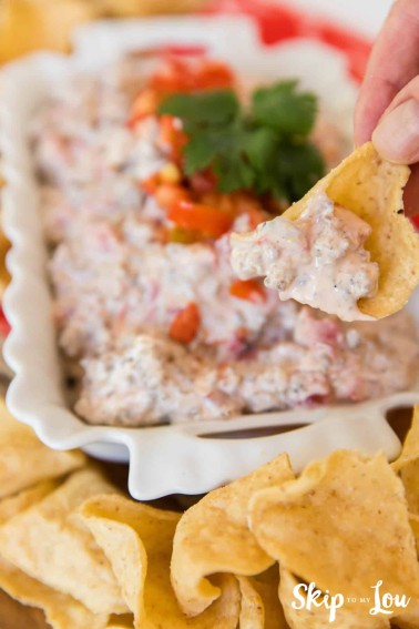 sausage rotel dip in white rectangle ceramic dish with hand holding chip scooping it up