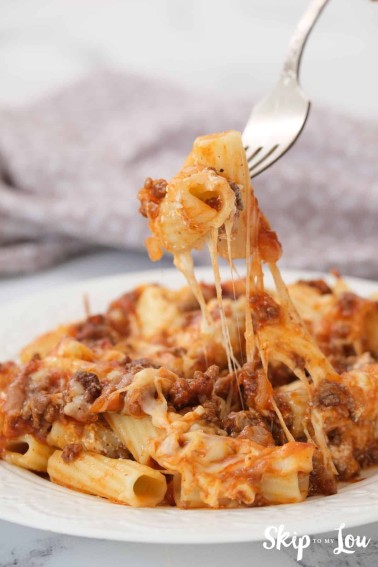 a plate of baked penne pasta with a fork removing a bite